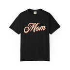 A black short-sleeve crewneck t-shirt featuring the word 'Mom' printed across the chest in a stylized beige cursive font with a red drop shadow, displayed on a clean white background.
