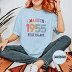 Person wearing a light blue t-shirt with 'Made in 1955 Built to Last' text, sitting on a patterned rug.