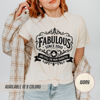 Person wearing a white t-shirt with 'Fabulous Since 2010' text design, plaid jacket, and jeans on a light gray background.