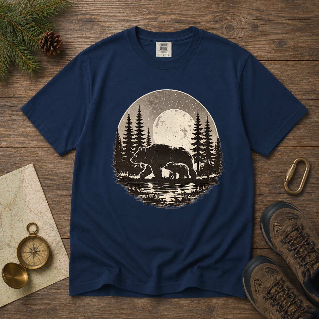 Navy blue t-shirt with bear and forest design on a wooden surface with nature-themed items.
