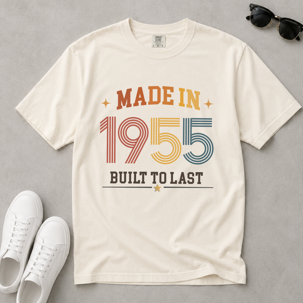 An off-white, ivory short-sleeve t-shirt with a retro-style graphic reading 'MADE IN 1955 BUILT TO LAST' in orange, red, yellow, and blue colors, styled in a flat-lay with white sneakers and sunglasses on a gray background. The perfect birthday gift for someone born in 1955.